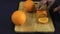 A juicy orange is cut into large round slices on a wooden Board. Strong hands, sharp knife. There is a tablecloth on the table.