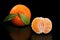 Juicy orange mandarin and half peeled mandarin on pure black background.