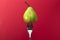 Juicy pear that has been stuck onto the end of a fork sitting in front of a vibrant red background.