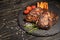 Juicy piece of fried meat lies on a stone plate against a black wooden table