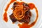Juicy piece of lamb under red sweet sauce and covered with fried onion on large round white plate on white background.