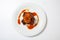 Juicy piece of lamb under red sweet sauce and covered with fried onion on large round white plate on white background.