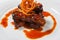 Juicy piece of lamb under red sweet sauce and covered with fried onion on large round white plate on white background.