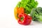 Juicy red and orange peppers with a green tail lies next to Bundle of lettuce and broccoli are on a white background