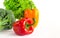 Juicy red and orange peppers with a green tail lies next to Bundle of lettuce and broccoli are on a white background