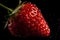 Juicy red strawberry with water droplets on a black background.