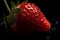 Juicy red strawberry with water droplets on a black background.