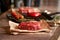 Juicy, seasoned raw ribeye steak on food paper, next to a grill pan, tomatoes on a branch, a head of garlic, red chili peppers