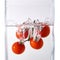 Juicy small cherry tomato dropped in water on white.