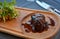 Juicy steak dish on wood plate with some greens on side in restaurant.