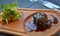 Juicy steak dish on wood plate with some greens on side in restaurant.