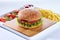 Juicy tasty hamburger on a wooden cutting board with french fried fries, vegetables and ketchup. Isolated composition on