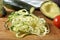 Julienned zucchini on a cutting board with tomato and avocado