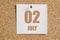 july 02. 02th day of the month, calendar date.White calendar sheet attached to brown cork board.Summer month, day of the