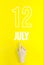 July 12nd. Day 12 of month, Calendar date.Hand finger pointing at a calendar date on yellow background.Summer month, day of the