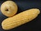 Jumbo sized corn and pear fruit on black leather board
