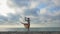 Jumping ballerina in beige silk dress and point on sand beach near sea at sunrise or sunset. Silhouette of young