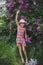 A jumping laughing girl of European appearance in a striped dress and a hat in a lilac garden