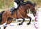 A jumping red sports horse with a bridle and a rider riding with his foot in a boot with a spur in a stirrup