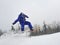 Jumping snowboarder keeps one hand on the snowboard on blue sky background