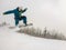 Jumping snowboarder keeps one hand on the snowboard on blue sky background