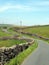 junction on a winding narrow country lane bordered by dry stone walls in hilly yorkshire dales countryside with blue summer sky