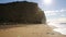 Jurassic coast Dorset at West Bay uk with sun shining on sandstone cliffs and distant man walking on beach by waves