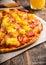 Just baked hawaiian pizza with freshly chopped pineapple and ham on the rustic wooden background. Selective focus