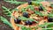 Just baked hot pizza on the black background close up. Vegetarian pizza with vegetables, black olives and fresh rucola