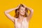 Just Happy. Joyful Teen Girl Touching Her Hair Standing Over Yellow Background