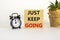 Just keep going symbol. Wooden blocks with words `Just keep going`. Beautiful white background, black alarm clock, house plant.
