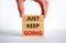 Just keep going symbol. Wooden blocks with words `Just keep going`. Beautiful white background, businessman hand. Business, just