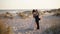 Just married couple hugging, expressing feelings at sandy coast at sunset. Young bride, groom enjoying summer evening on