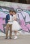 Just married loving hipster couple in wedding dress and suit outdoor in city setting against colorful graffiti wall.