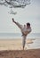 Karate man in an old kimono and black belt training high kick at the sea. Martial arts concept.