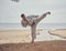 Karate man in an old kimono and black belt training side kick at the sea. Martial arts concept.