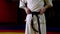 Karate master in kimono ties black belt on waist in dark gym