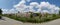 Karnal, India - April 18, 2019: A wide panoramic landscape shot with blue sky, clouds, trees, and trucks crossing an underpass.