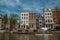 Kayak paddler on tree-lined canal with brick buildings and blue sky in Amsterdam.