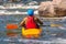 A kayaker with oars in full gear is sitting in a kayak on white water. Back view