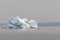 Kayakers paddle near a large iceberg on a hazy day