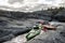 Kayaks stand moored on a rocky shore, in the background there is