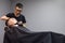 Kazakh barber shaves beard with a razor to a client in a barbershop, a young guy is doing a beard haircut against a gray wall,