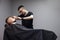 Kazakh barber shaves beard with a razor to a client in a barbershop, a young guy is doing a beard haircut against a gray wall,