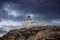 Kea island, Greece. Lighthhouse Tamelos on a rocky cliff, cloudy sky background