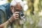 A keen gray-haired man photographs flowers in the garden. Hobby grandfather on summer vacation