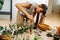 Keen woman in living room planting inside glass bottle, using stick