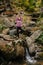 Keen woman staing on one leg on big stone, doing yoga over mountain spring