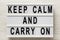 `Keep calm and carry on` words on a lightbox on a white wooden background, top view. Overhead, from above, flat lay