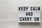 `Keep calm and carry on` words on a modern board on a white wooden surface, top view. Overhead, from above, flat lay. Copy space